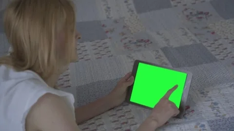 Beautiful girl using tablet pc with pre-keyed green screen lying on bed Stock Footage 63521054