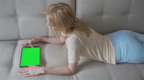 Beautiful girl using tablet pc with pre-keyed green screen laying on sofa Stock Footage 63521059