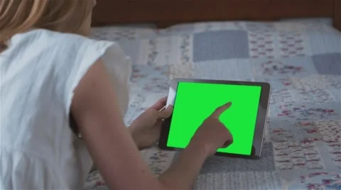 Beautiful girl using tablet pc with pre-keyed green screen lying on bed Stock Footage 63521234