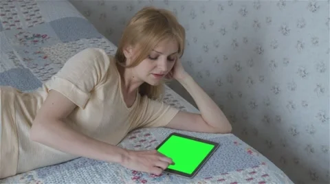 Beautiful girl using tablet pc with pre-keyed green screen lying on bed Stock Footage 63521297