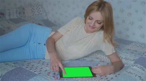Beautiful girl using tablet pc with pre-keyed green screen lying on bed Stock Footage 63522140