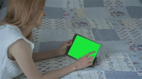 Beautiful girl using tablet pc with pre-keyed green screen lying on bed Stock Footage 63523409