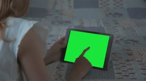 Beautiful girl using tablet pc with pre-keyed green screen lying on bed Stock Footage 63523755