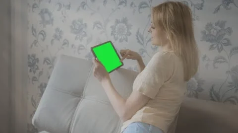 Beautiful girl using tablet pc with pre-keyed green screen sitting on sofa Stock Footage 63523806