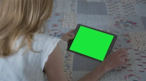 Beautiful girl using tablet pc with pre-keyed green screen lying on bed at home Stock Footage 63524158