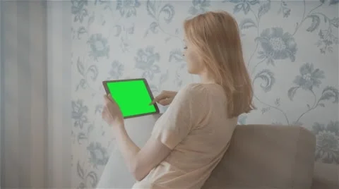 Beautiful girl using tablet pc with pre-keyed green screen sitting on sofa Stock Footage 63525182