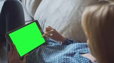 Beautiful girl using tablet pc with pre-keyed green screen laying on sofa 3 Stock Footage 64694933