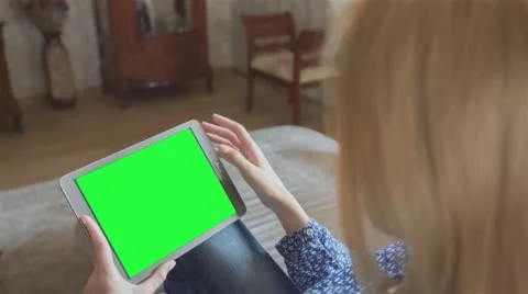 Beautiful girl using tablet pc with pre-keyed green screen sitting on sofa Stock Footage 64698537