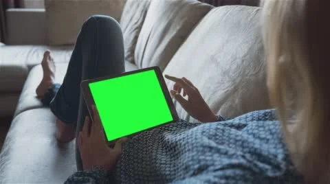Beautiful girl using tablet pc with pre-keyed green screen laying on sofa Stock Footage 64699225