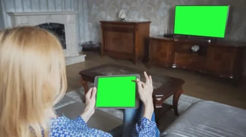 Beautiful girl using tablet pc with pre-keyed green screen sitting on sofa Video stock 64700496