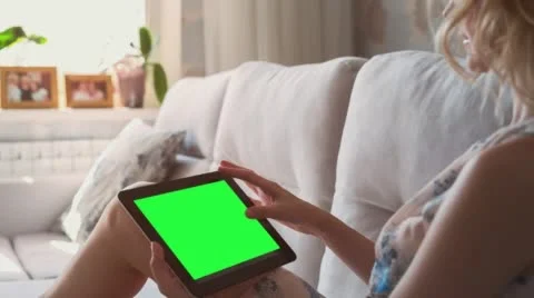 Beautiful girl using tablet pc with pre-keyed green screen laying on sofa at Stock Footage 64985949