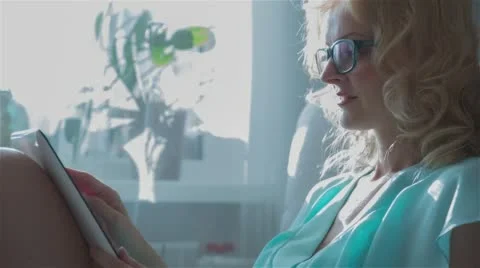 Beautiful girl using Tablet PC sitting on sofa near window 5 Stock Footage 65747860