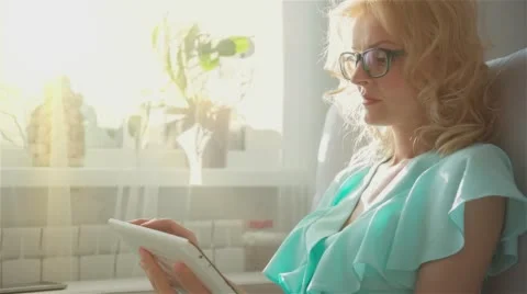 Beautiful girl using Tablet PC sitting on sofa near window 4 Stock Footage 65748260