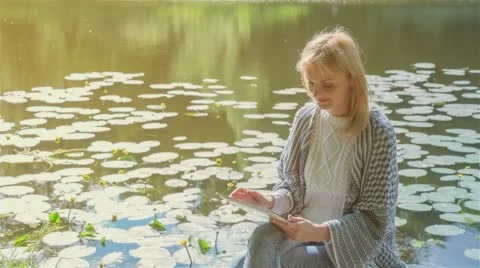 Beautiful girl using Tablet PC sitting near lake in city park 2 on sunset Stock Footage 66146539