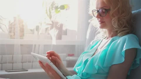 Beautiful girl using Tablet PC sitting on sofa near window 7 Stock Footage 66251136