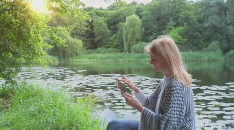 Beautiful girl using Tablet PC sitting near lake in city park 3 on sunset Stock Footage 66382009