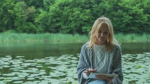 Beautiful girl using Tablet PC sitting near lake in city park. Stock Footage 66646905