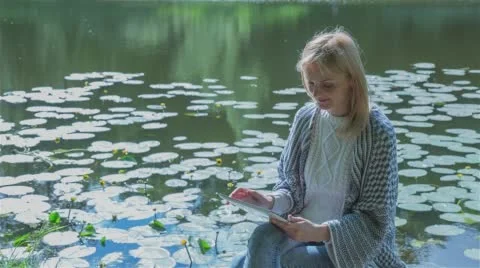 Beautiful girl using Tablet PC sitting near lake in city park. Stock Footage 66647562