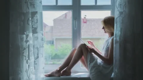 Beautiful Girl Using Tablet PC Sitting on Window Edge Stock Footage 67104580