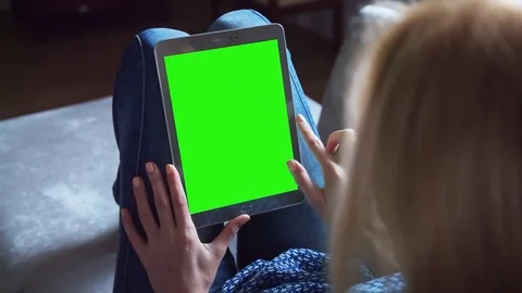 Beautiful girl using tablet pc with pre keyed green screen sitting on sofa Stock Footage 72520571