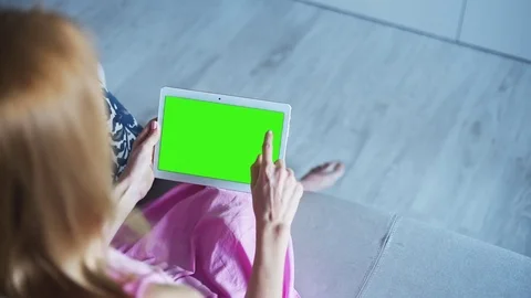 Beautiful girl using tablet pc with pre keyed green screen sitting on sofa Stock Footage 72523398