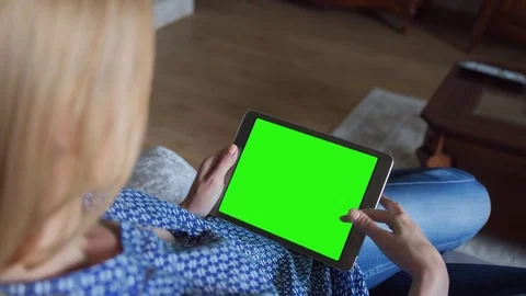 Beautiful girl using tablet pc with pre keyed green screen sitting on sofa Stock Footage 72529422