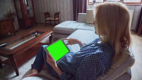 Beautiful girl using tablet pc with pre keyed green screen sitting on sofa Stock Footage 72762632