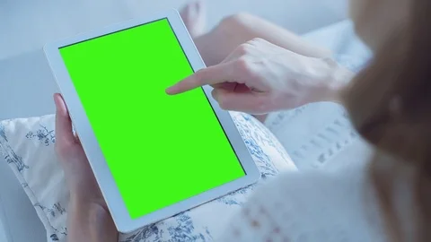 Beautiful girl using tablet pc with pre-keyed green screen sitting on sofa Stock Footage 73783807