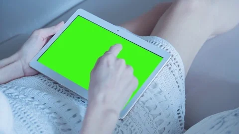 Beautiful girl using tablet pc with pre-keyed green screen sitting on sofa Video stock 73784029