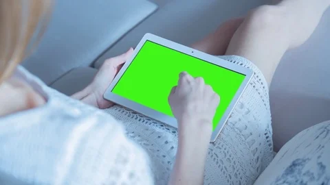 Beautiful girl using tablet pc with pre-keyed green screen sitting on sofa Stock Footage 73784590