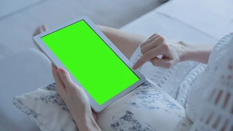 Beautiful girl using tablet pc with pre-keyed green screen sitting on sofa Stock Footage 73844730