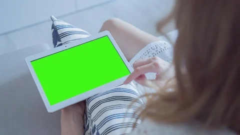 Beautiful girl using tablet pc with pre-keyed green screen sitting on sofa Stock Footage 74142740