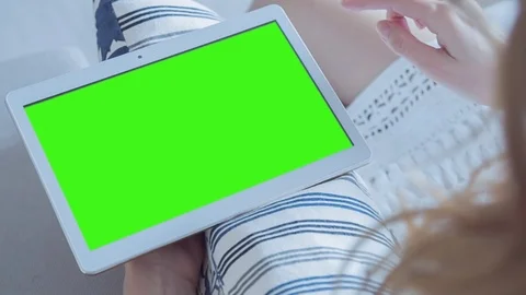 Beautiful girl using tablet pc with pre-keyed green screen sitting on sofa Stock Footage 74214478