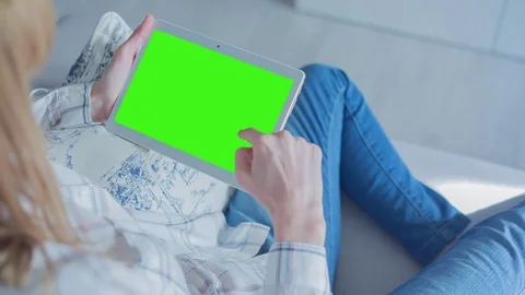 Beautiful girl using tablet pc with Pre-Keyed Green Screen sitting on sofa Video stock 75044702