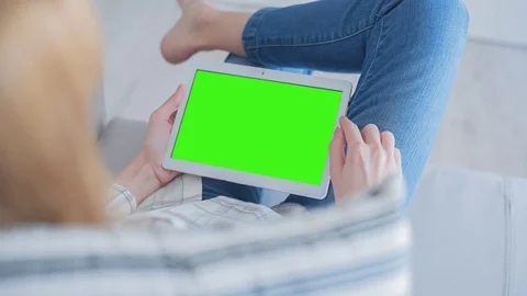 Beautiful girl using tablet pc with Pre-Keyed Green Screen sitting on sofa Video stock 75277937