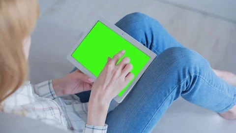 Beautiful girl using tablet pc with Pre-Keyed Green Screen sitting on sofa Video stock 75377671