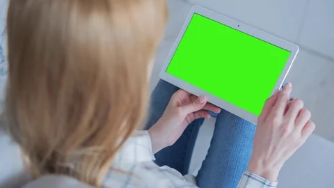 Beautiful girl using tablet pc with Pre-Keyed Green Screen sitting on sofa Video stock 75381094