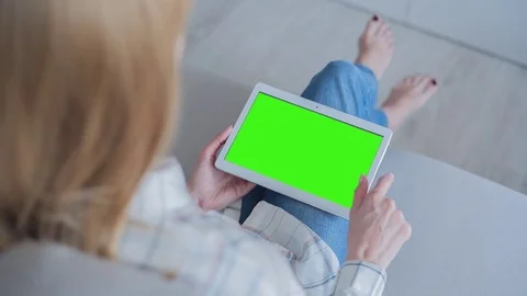 Beautiful girl using tablet pc with Pre-Keyed Green Screen sitting on sofa Video stock 75627055