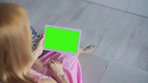 Beautiful girl using tablet pc with Pre-Keyed Green Screen sitting on sofa Stock Footage 80829297