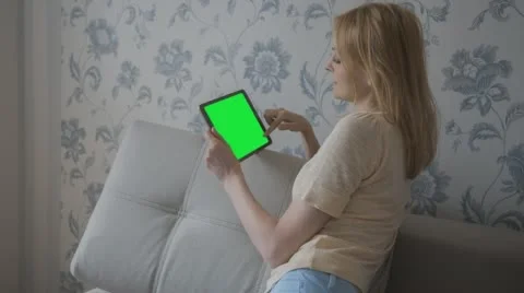 Beautiful girl using tablet with pre-keyed green screen sitting on sofa at home Stock Footage 63655347