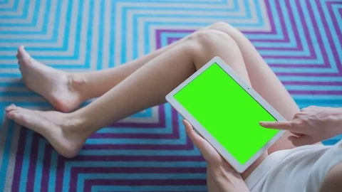 Beautiful girl in white top sitting on the pattern floor uses Tablet PC Stock Footage 77046292