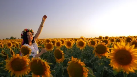 Beautiful girl with wreath running on yellow sunflower field, raising hands Stock Footage