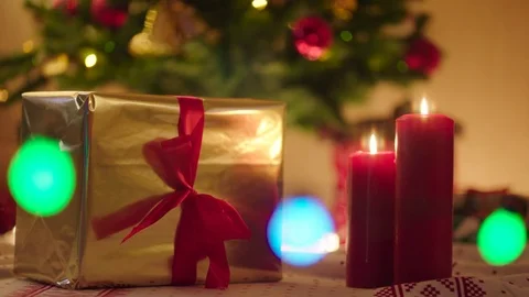 Beautiful gold gift box with red ribbon and burning candles on Christmas night Stock Footage 73896159
