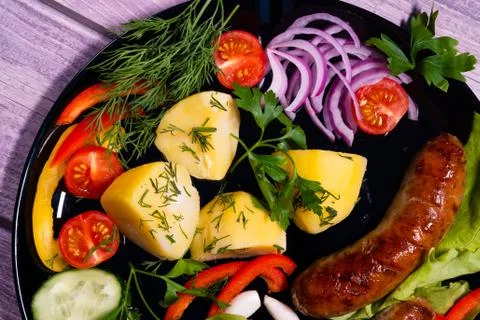 Beautiful grilled sausages on a black plate with vegetables and. Stock Photos
