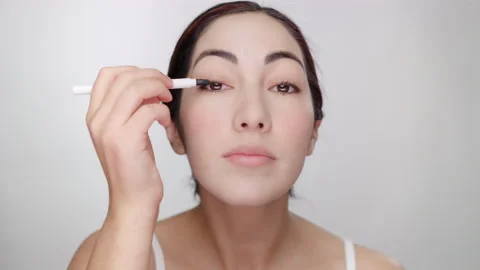 Beautiful hispanic model blends eyeliner with applicator while looking at camera Stock Footage 193623991