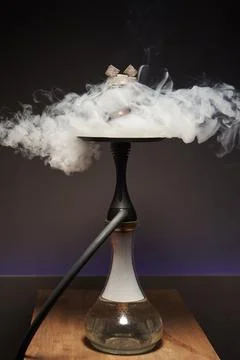 Beautiful hookah with a transparent flask in a cloud of white smoke on a saucer Stock Photos