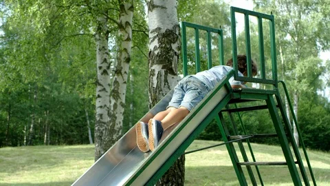 Beautiful kid sliding down in a reverse way during a bright day at the park Vídeo Stock 98564192