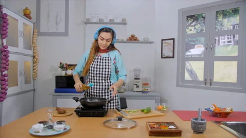 A beautiful lady heating oil in a pan while enjoying music in the kitchen Stock Footage 156432905
