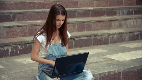 Beautiful lady with the laptop sitting on the stairs outdoors Stock Footage