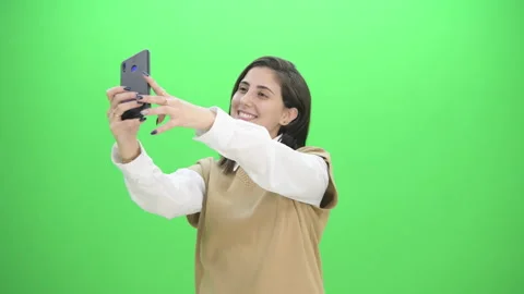 Beautiful lady taking selfies while smiling and fixing her hair on green screen Stock Footage 170704139